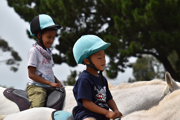 Two students from the community outreach program side-by-side on horseback during a group session at EQuivalence in Durbanville.
