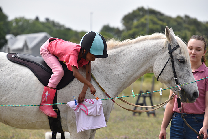 A student in the EQuivalence community program practicing fine motor skills by clipping a peg on a line while mounted, guided by a facilitator in Durbanville.