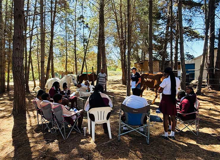 Students standing quietly in a circle around a horse during a reflection exercise at EQuivalence.
